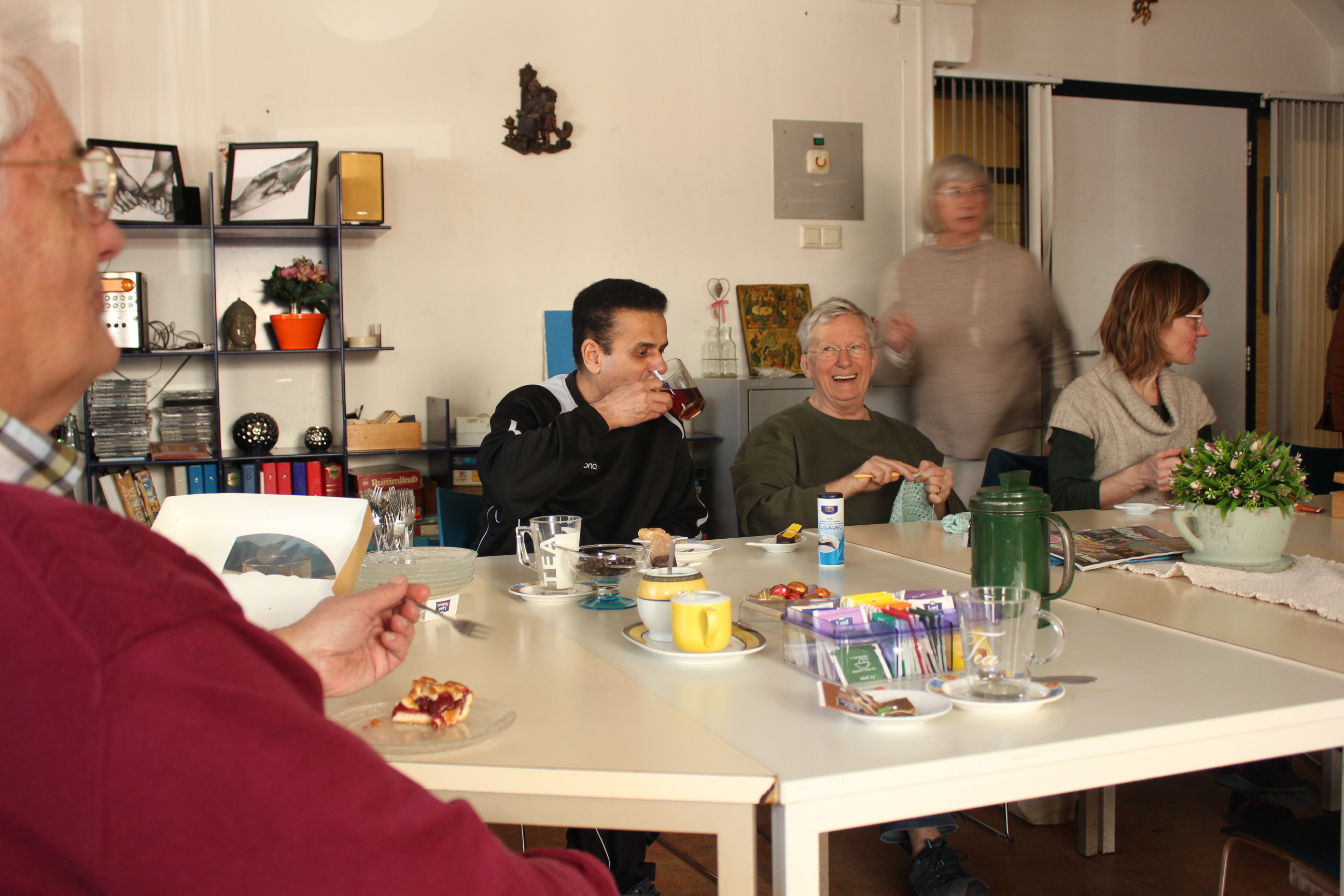 Mensen aan tafel die met elkaar praten, één persoon drinkt thee