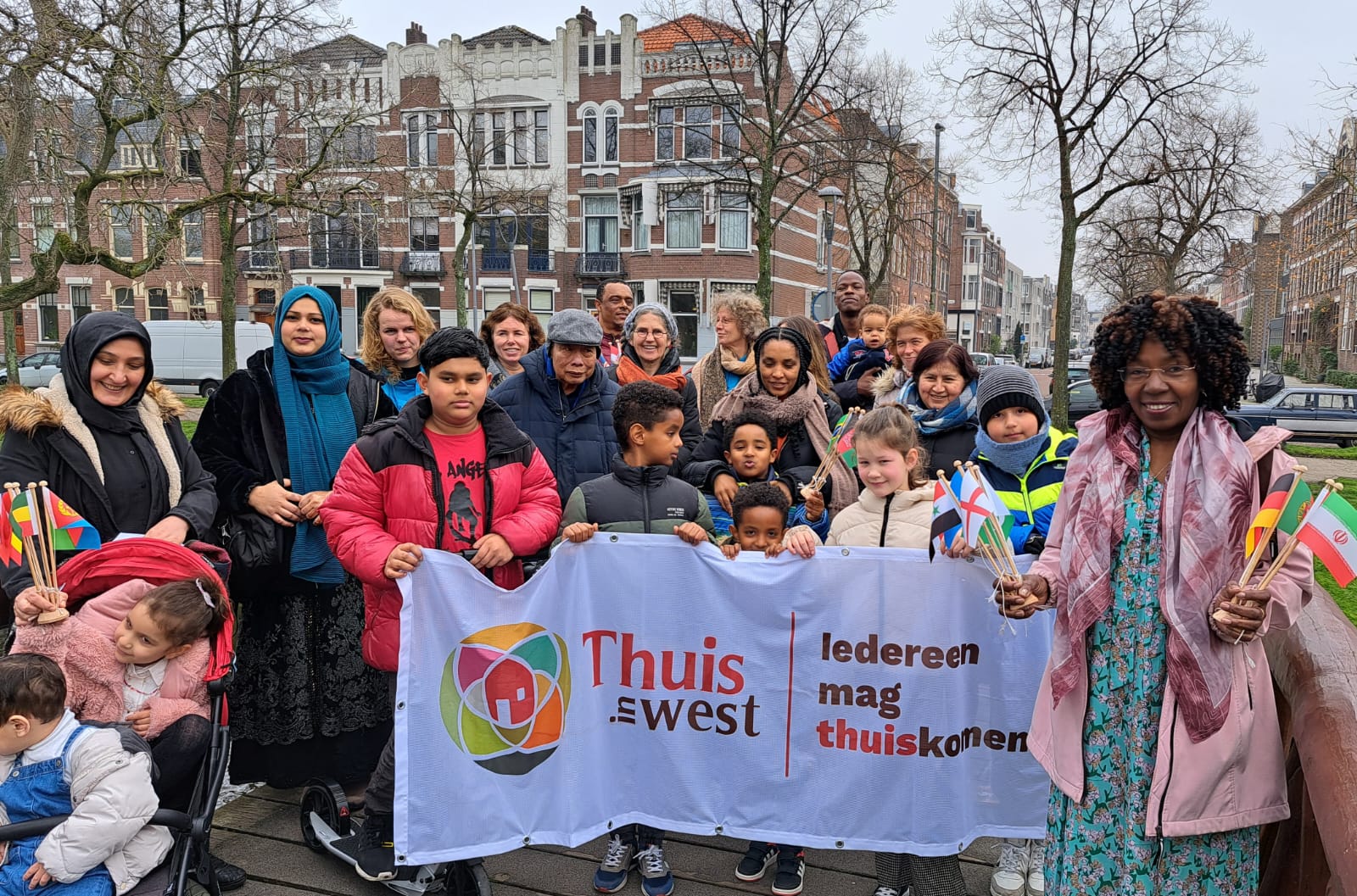 Groep vrouwen en kinderen houden buiten een banner vast met de tekst ''Thuis in West''