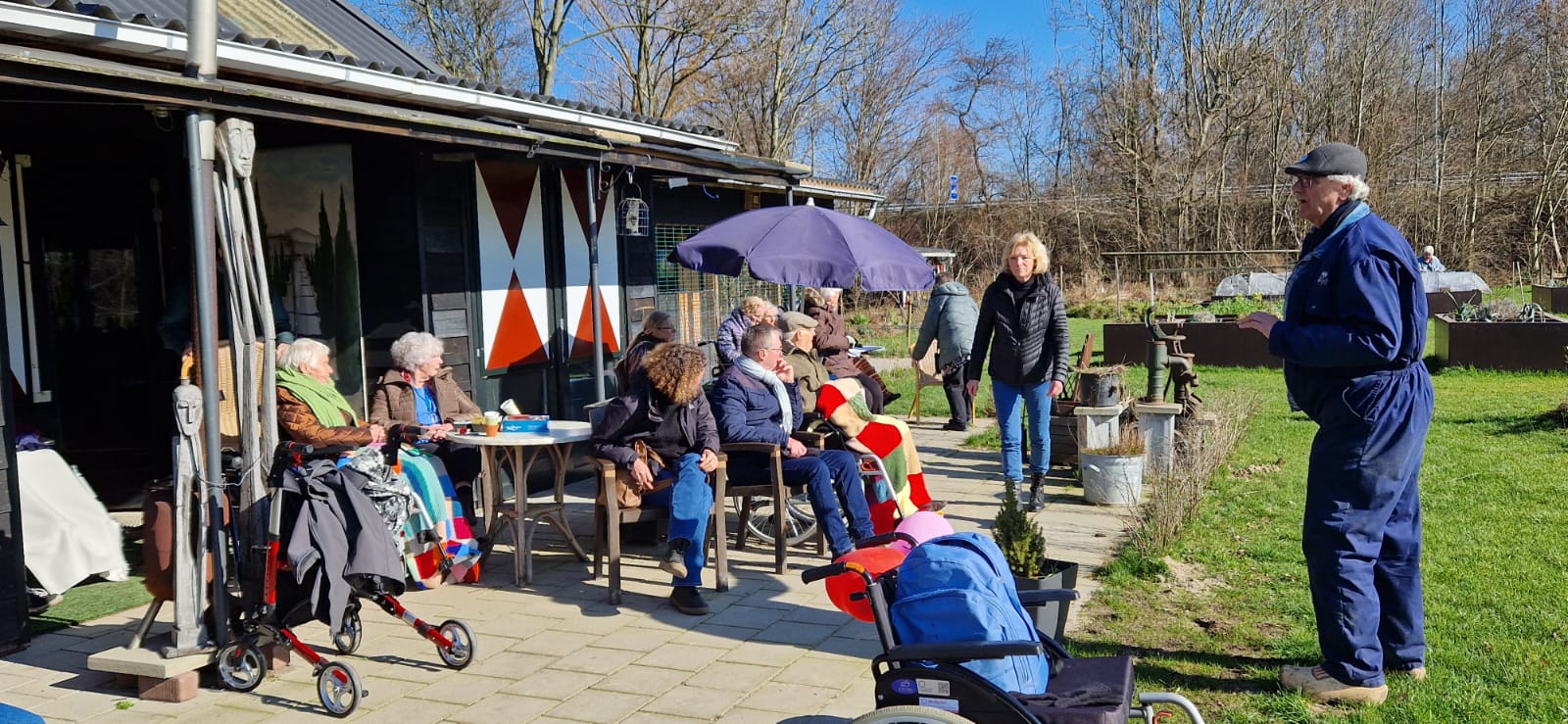 Moestuin de Terp Groep mensen in de tuin, naast hen is een paarse parasol