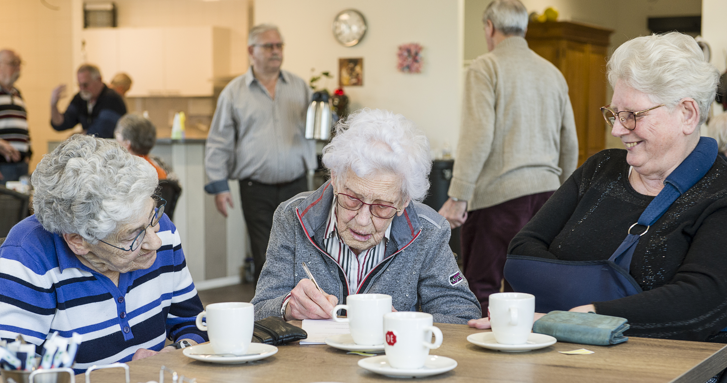 Surplus Drie dames drinken een kopje koffie. De dame in het midden is aan het schrijven.