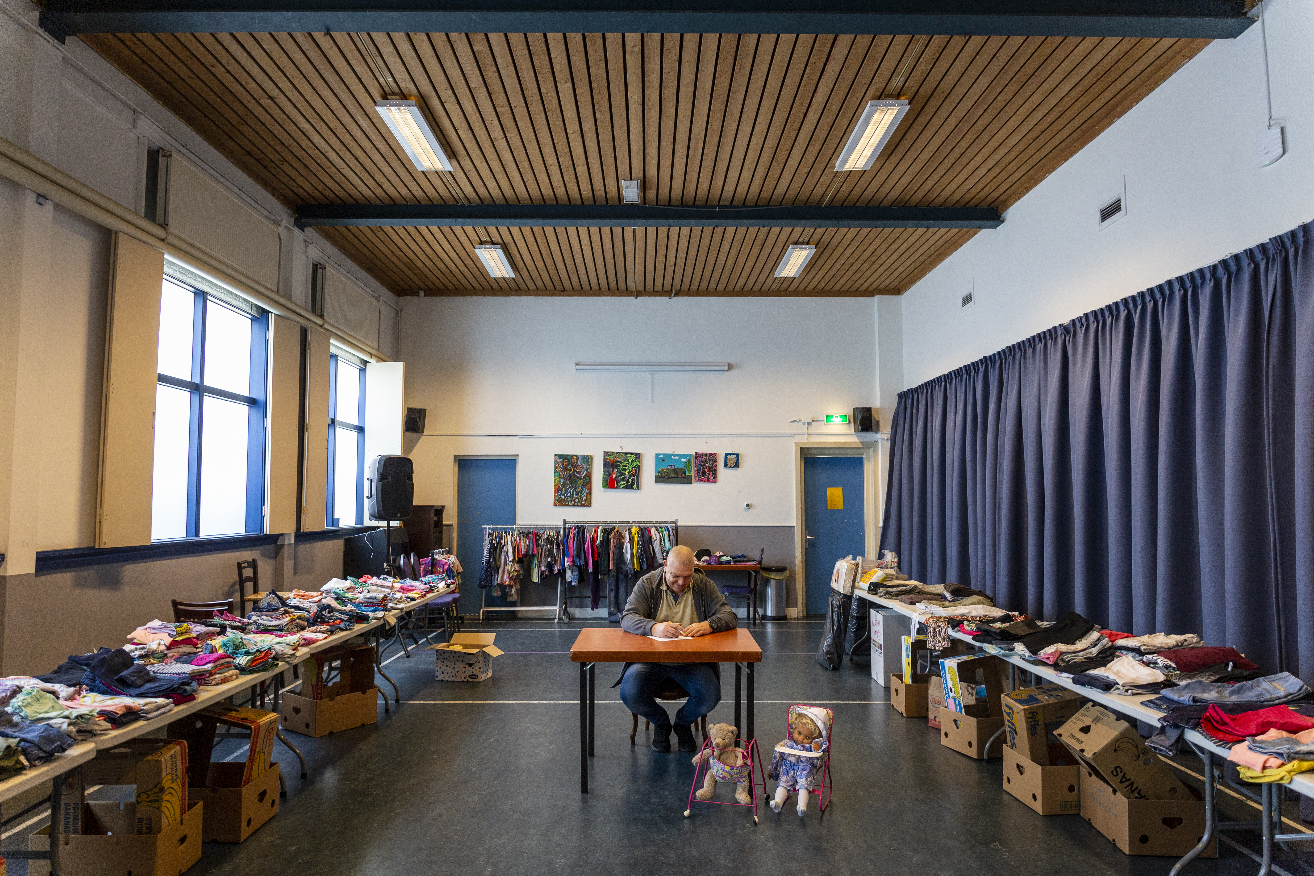 Stichting De Geus Man zit in het midden van een gymzaal omringd door kleding